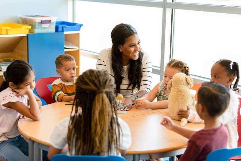 speech-delay-symptoms Teacher sits at table with young children providing early learning while using a three dimensional diagram of the solar system as a teaching aid