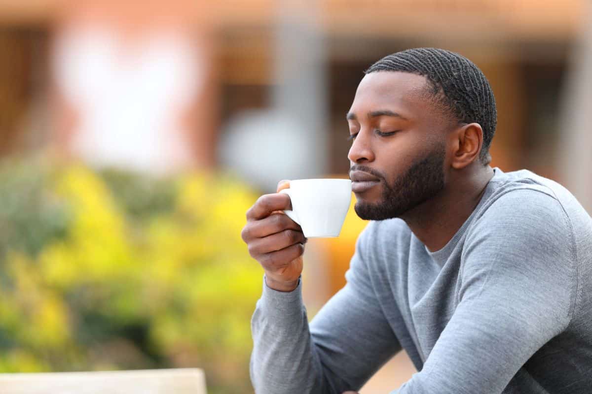 Nose-Loss-of-Smell Man smelling a cup of coffee in an outdoor setting containing a bush of yellow flowers and a blurry storefront
